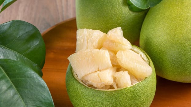 Fresh peeled pomelo, grapefruit, shaddock with green leaves on dark wooden plank table. Seasonal fruit near mid-autumn festival, close up, copy space