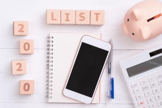 2020 goal, finance plan abstract design concept, wood blocks on white table background with piggy bank, cell phone, top view, flat lay, copy space.