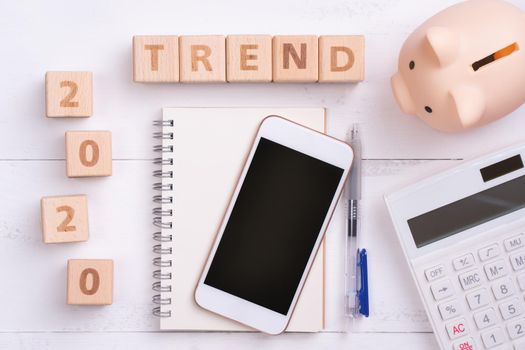 2020 goal, finance plan abstract design concept, wood blocks on white table background with piggy bank, cell phone, top view, flat lay, copy space.