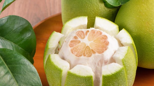 Fresh peeled pomelo, grapefruit, shaddock with green leaves on dark wooden plank table. Seasonal fruit near mid-autumn festival, close up, copy space