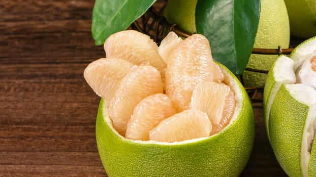 Fresh peeled pomelo, grapefruit, shaddock with green leaves on dark wooden plank table. Seasonal fruit near mid-autumn festival, close up, copy space