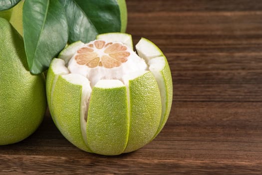 Fresh peeled pomelo, grapefruit, shaddock with green leaves on dark wooden plank table. Seasonal fruit near mid-autumn festival, close up, copy space