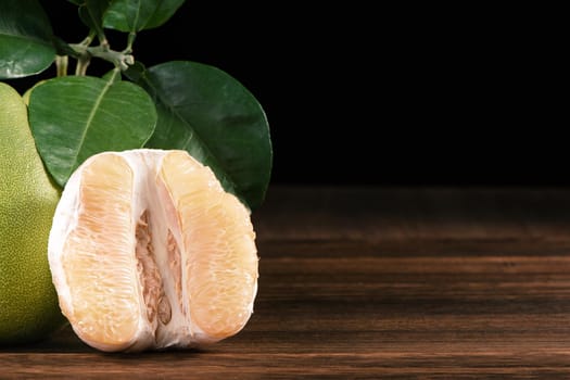 Fresh peeled pomelo, grapefruit, shaddock with green leaves on dark wooden plank table. Seasonal fruit near mid-autumn festival, close up, copy space