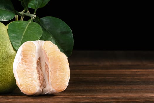 Fresh peeled pomelo, grapefruit, shaddock with green leaves on dark wooden plank table. Seasonal fruit near mid-autumn festival, close up, copy space