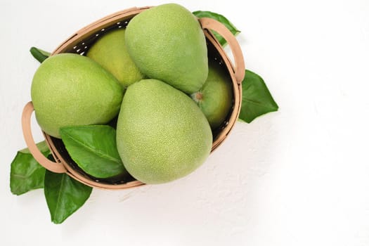 Fresh pomelo, pummelo, grapefruit, shaddock on white cement background in bamboo basket. Autumn seasonal fruit, top view, flat lay, tabletop shot.