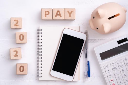 2020 goal, finance plan abstract design concept, wood blocks on white table background with piggy bank, cell phone, top view, flat lay, copy space.