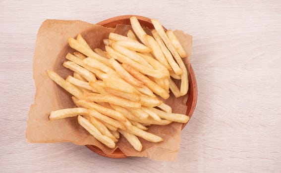 Golden yummy deep French fries on kraft baking sheet paper and serving tray to eat with ketchup and yellow mustard, top view, lifestyle.