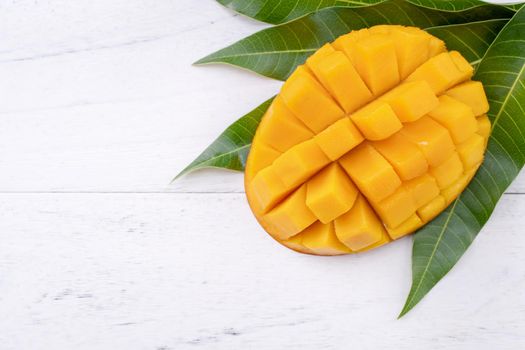 Beautiful chopped ripe mango with green leaves on bright white color wooden background, top view, flat lay, copy space. Tropical fruit design concept.