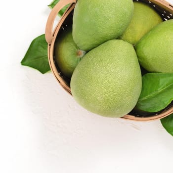 Fresh pomelo, pummelo, grapefruit, shaddock on white cement background in bamboo basket. Autumn seasonal fruit, top view, flat lay, tabletop shot.