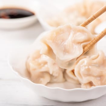 Fresh, delicious boiled pork, shrimp gyoza dumplings on white background with soy sauce and chopsticks, close up, lifestyle. Homemade design concept.