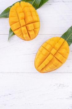 Beautiful chopped ripe mango with green leaves on bright white color wooden background, top view, flat lay, copy space. Tropical fruit design concept.