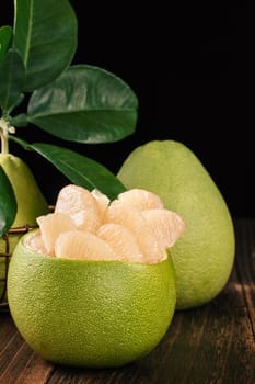 Fresh peeled pomelo, grapefruit, shaddock with green leaves on dark wooden plank table. Seasonal fruit near mid-autumn festival, close up, copy space