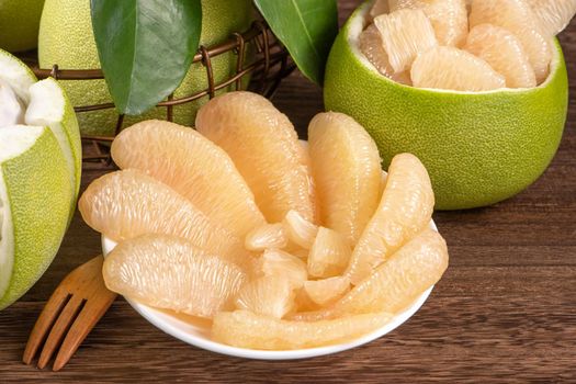 Fresh peeled pomelo, grapefruit, shaddock with green leaves on dark wooden plank table. Seasonal fruit near mid-autumn festival, close up, copy space