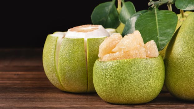Fresh peeled pomelo, grapefruit, shaddock with green leaves on dark wooden plank table. Seasonal fruit near mid-autumn festival, close up, copy space