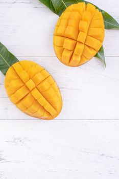 Beautiful chopped ripe mango with green leaves on bright white color wooden background, top view, flat lay, copy space. Tropical fruit design concept.