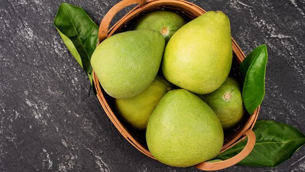 Fresh peeled pomelo, pummelo, grapefruit, shaddock on dark background in bamboo basket. Autumn seasonal fruit, top view, flat lay, tabletop shot.