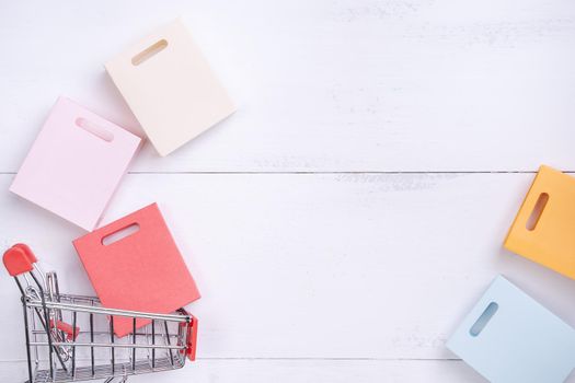 Abstract design element,annual sale,shopping season concept,mini cart with colorful paper bag on white wooden table background,top view,flat lay