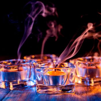 Halloween concept, spooky decorations with lighting up candle and candle holder with blue tone smoke around on a dark wooden table, close up.