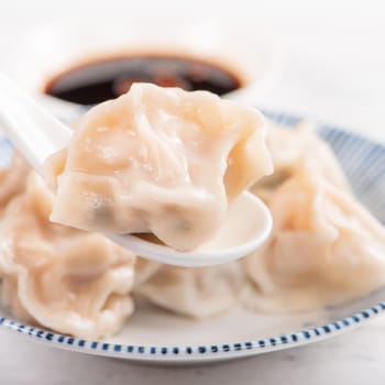 Fresh, delicious boiled pork, shrimp gyoza dumplings on white background with soy sauce and chopsticks, close up, lifestyle. Homemade design concept.