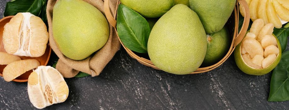 Fresh peeled pomelo, pummelo, grapefruit, shaddock on dark background in bamboo basket. Autumn seasonal fruit, top view, flat lay, tabletop shot.