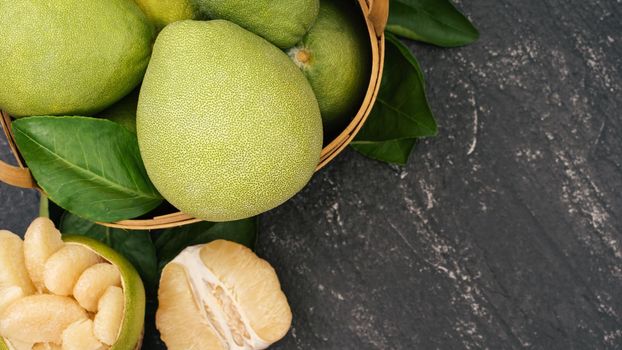 Fresh peeled pomelo, pummelo, grapefruit, shaddock on dark background in bamboo basket. Autumn seasonal fruit, top view, flat lay, tabletop shot.