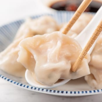 Fresh, delicious boiled pork, shrimp gyoza dumplings on white background with soy sauce and chopsticks, close up, lifestyle. Homemade design concept.