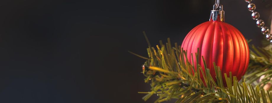 Beautiful Christmas decor concept, bauble hanging on the Christmas tree with sparkling light spot, blurry dark black background, macro detail, close up.