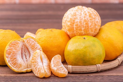 Peeled tangerines in a bamboo sieve basket on dark wooden table with red brick wall background, Chinese lunar new year fruit design concept, close up.
