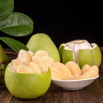 Fresh peeled pomelo, grapefruit, shaddock with green leaves on dark wooden plank table. Seasonal fruit near mid-autumn festival, close up, copy space