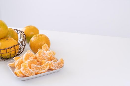 Beautiful peeled tangerines in a plate and metal basket isolated on bright white clean table in a modern contemporary kitchen island, close up.