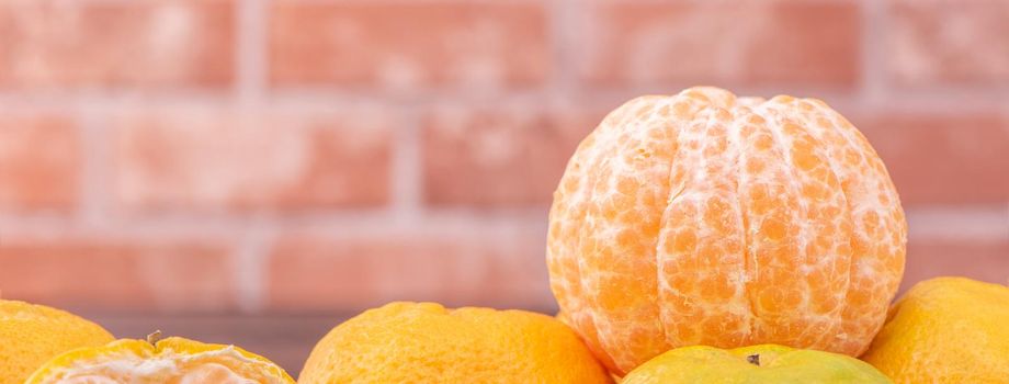 Peeled tangerines in a bamboo sieve basket on dark wooden table with red brick wall background, Chinese lunar new year fruit design concept, close up.