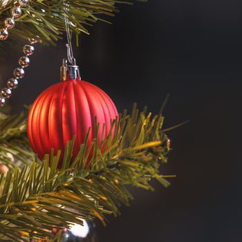 Beautiful Christmas decor concept, bauble hanging on the Christmas tree with sparkling light spot, blurry dark black background, macro detail, close up.