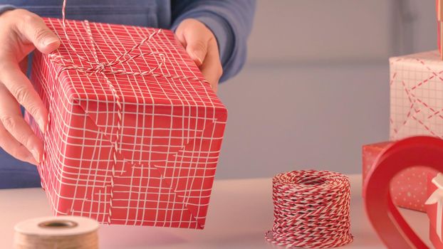 A young woman in blue is wrapping, packaging Christmas gift for kids children by beautiful, red, white wrapper with glittering light, lifestyle.