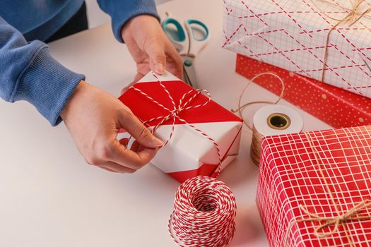 A young woman in blue is wrapping, packaging Christmas gift for kids children by beautiful, red, white wrapper with glittering light, lifestyle.