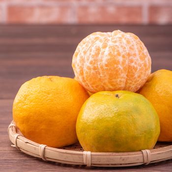 Peeled tangerines in a bamboo sieve basket on dark wooden table with red brick wall background, Chinese lunar new year fruit design concept, close up.