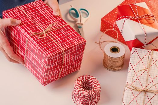 A young woman in blue is wrapping, packaging Christmas gift for kids children by beautiful, red, white wrapper with glittering light, lifestyle.