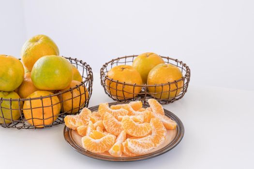 Beautiful peeled tangerines in a plate and metal basket isolated on bright white clean table in a modern contemporary kitchen island, close up.