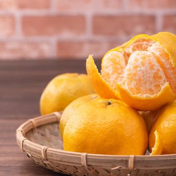 Peeled tangerines in a bamboo sieve basket on dark wooden table with red brick wall background, Chinese lunar new year fruit design concept, close up.