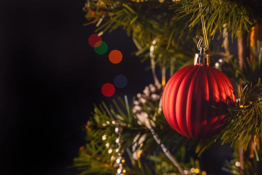 Beautiful Christmas decor concept, bauble hanging on the Christmas tree with sparkling light spot, blurry dark black background, macro detail, close up.