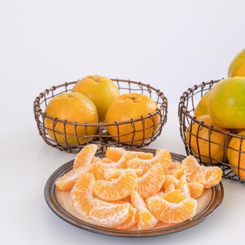 Beautiful peeled tangerines in a plate and metal basket isolated on bright white clean table in a modern contemporary kitchen island, close up.