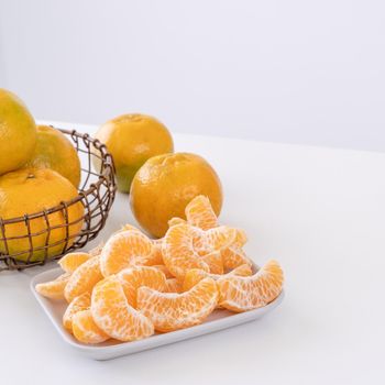 Beautiful peeled tangerines in a plate and metal basket isolated on bright white clean table in a modern contemporary kitchen island, close up.