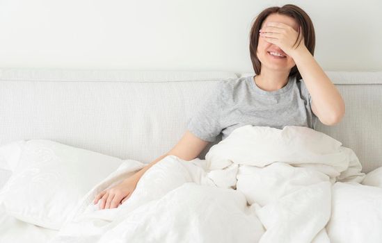 Pretty young woman smiling, sitting on the bed. Happy lady enjoying morning and laughing, copy space