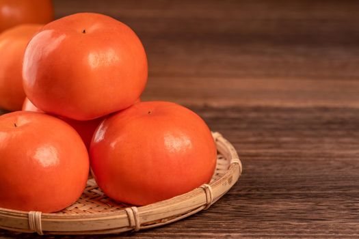 Sliced sweet persimmon kaki in a bamboo sieve basket on dark wooden table with red brick wall background, Chinese lunar new year fruit design concept, close up.