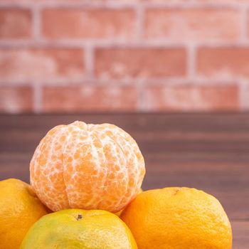 Peeled tangerines in a bamboo sieve basket on dark wooden table with red brick wall background, Chinese lunar new year fruit design concept, close up.