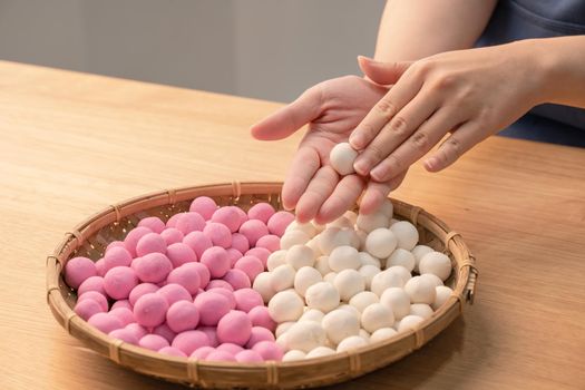 An Asia woman is making Tang yuan, yuan xiao, Chinese traditional food rice dumplings in red and white for lunar new year, winter festival, close up.