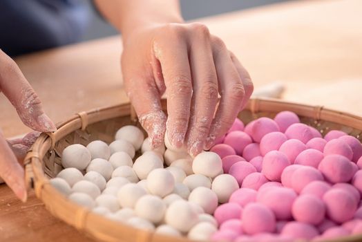 An Asia woman is making Tang yuan, yuan xiao, Chinese traditional food rice dumplings in red and white for lunar new year, winter festival, close up.