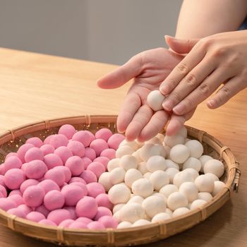 An Asia woman is making Tang yuan, yuan xiao, Chinese traditional food rice dumplings in red and white for lunar new year, winter festival, close up.