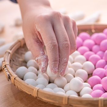 An Asia woman is making Tang yuan, yuan xiao, Chinese traditional food rice dumplings in red and white for lunar new year, winter festival, close up.