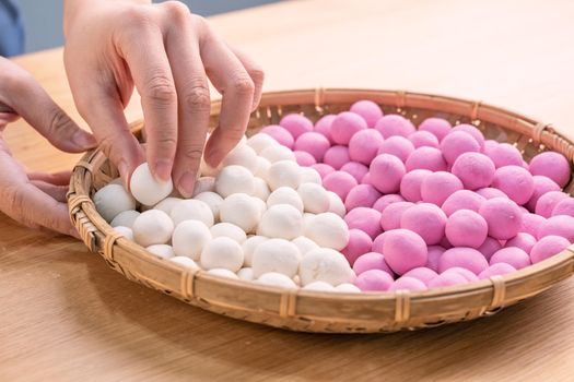 An Asia woman is making Tang yuan, yuan xiao, Chinese traditional food rice dumplings in red and white for lunar new year, winter festival, close up.