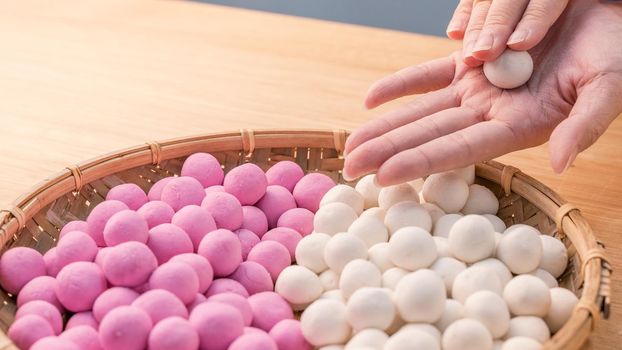 An Asia woman is making Tang yuan, yuan xiao, Chinese traditional food rice dumplings in red and white for lunar new year, winter festival, close up.